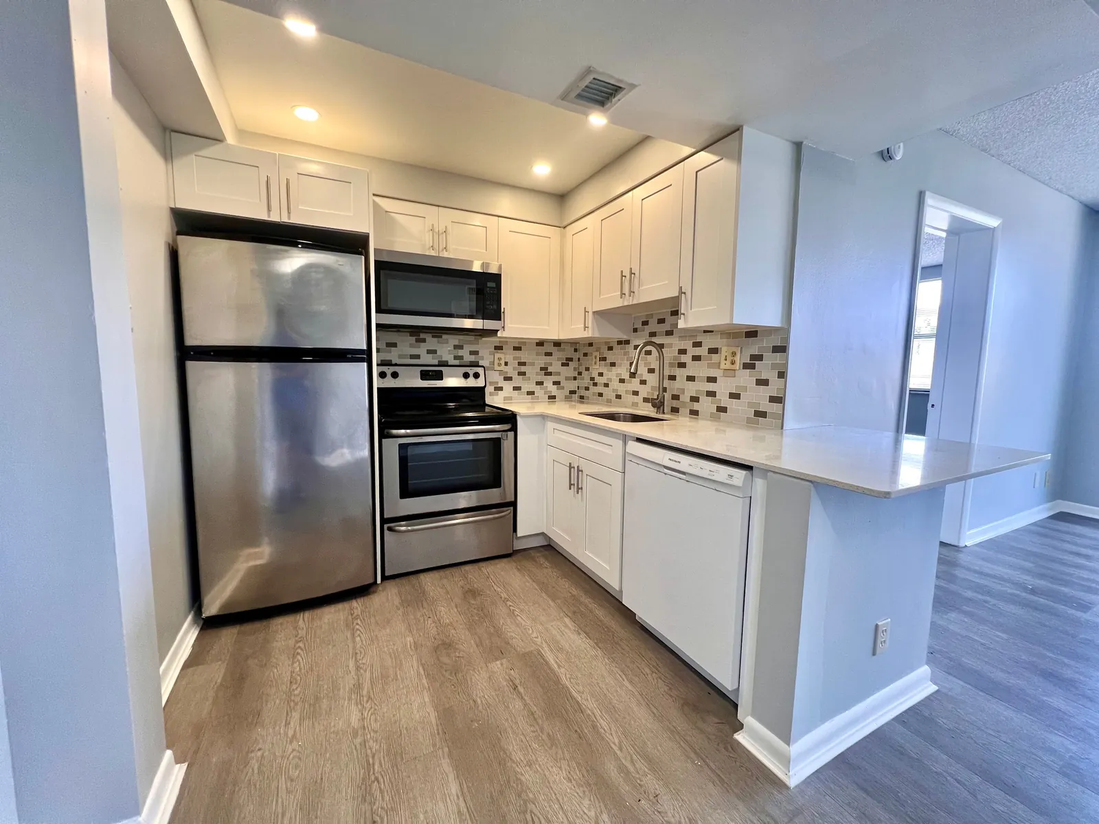 White kitchen with mosaic backsplash, peninsula and stainless appliances in Miami
