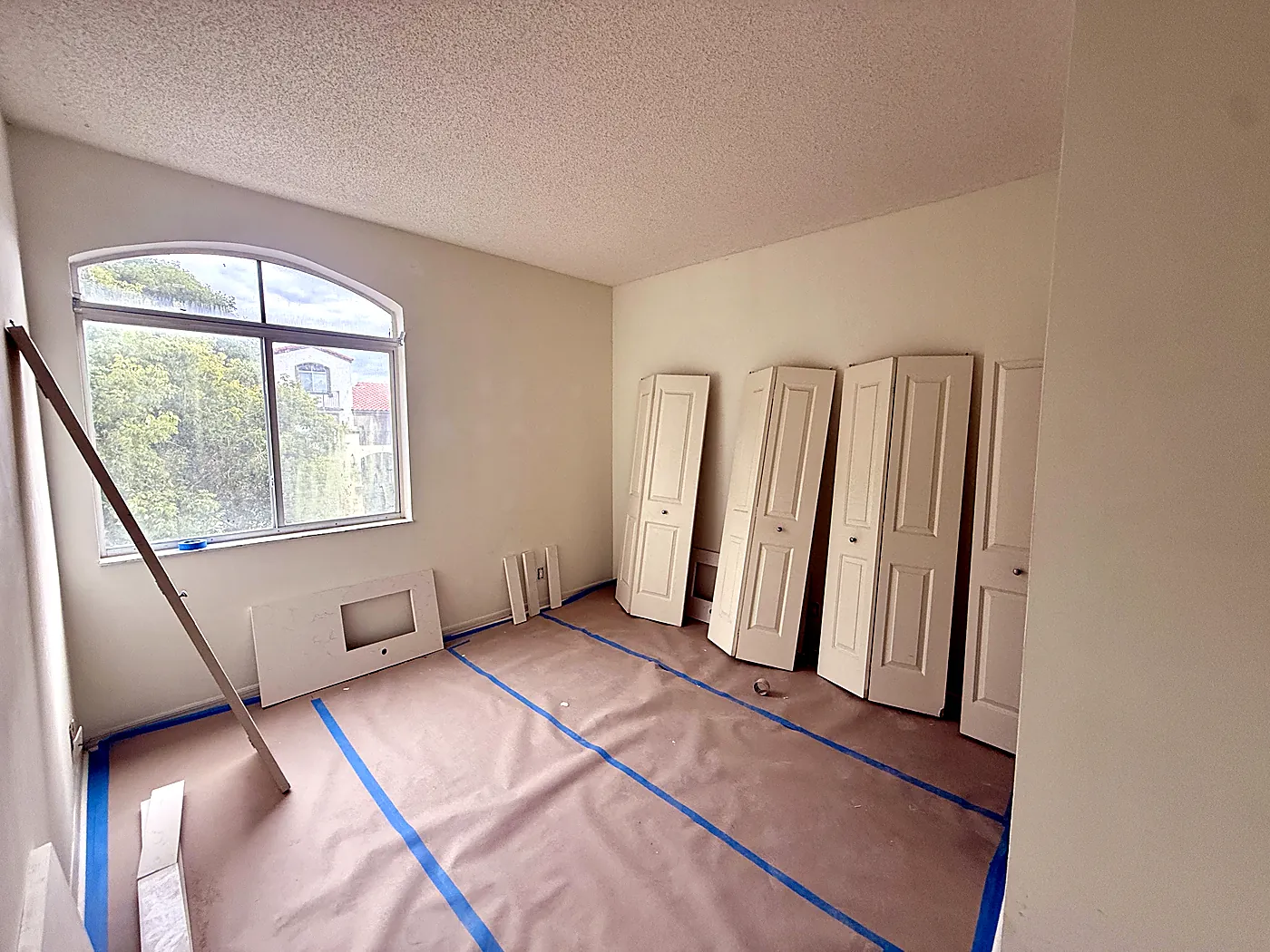 Bedroom masked and floor covered before painting, with closet doors removed for spray finishing in Miami